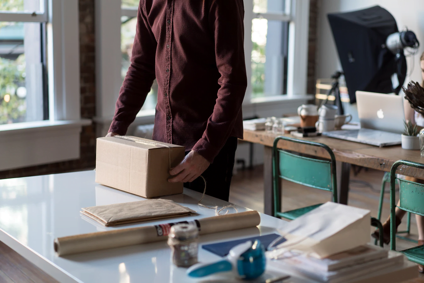 man in a burgundy shirt wrapping up a box with a piece of string