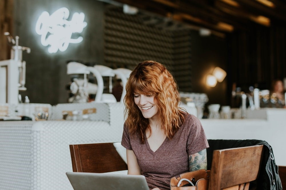 smiling woman with red hair typing on her laptop